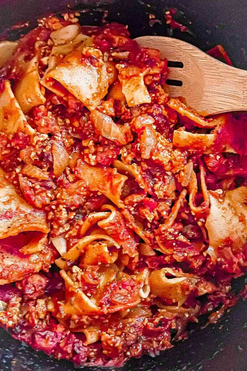 Completed Bolognese sauce with cooked whole wheat noodles are in the cast iron Dutch oven with a wooden spoon.