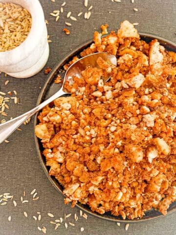 Prepared tofu sausage crumbles in a dish on counter surrounded by fennel seeds.