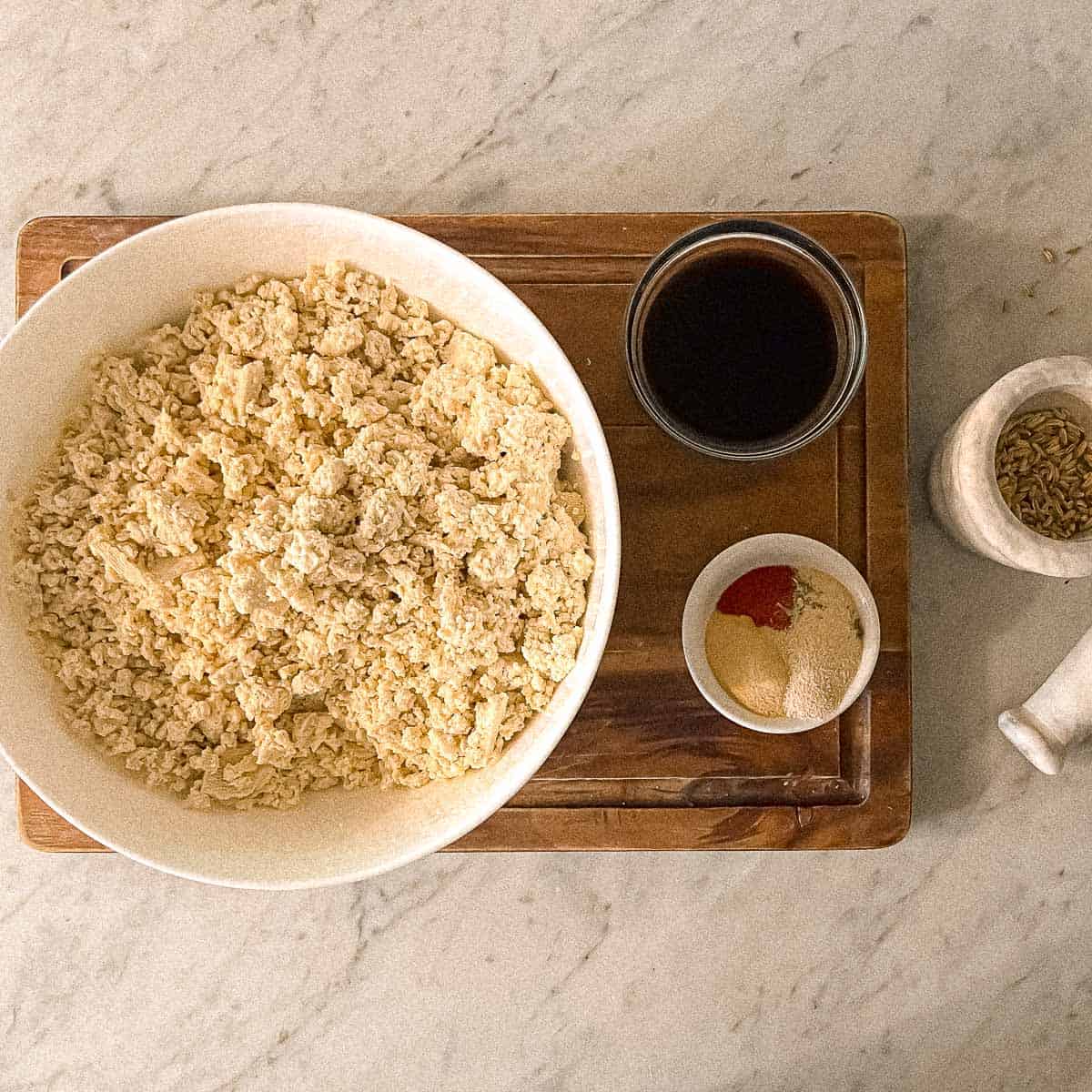 Crumbled tofu in a mixing bowl flanked by Italian tofu sausage seasonings on a counter.