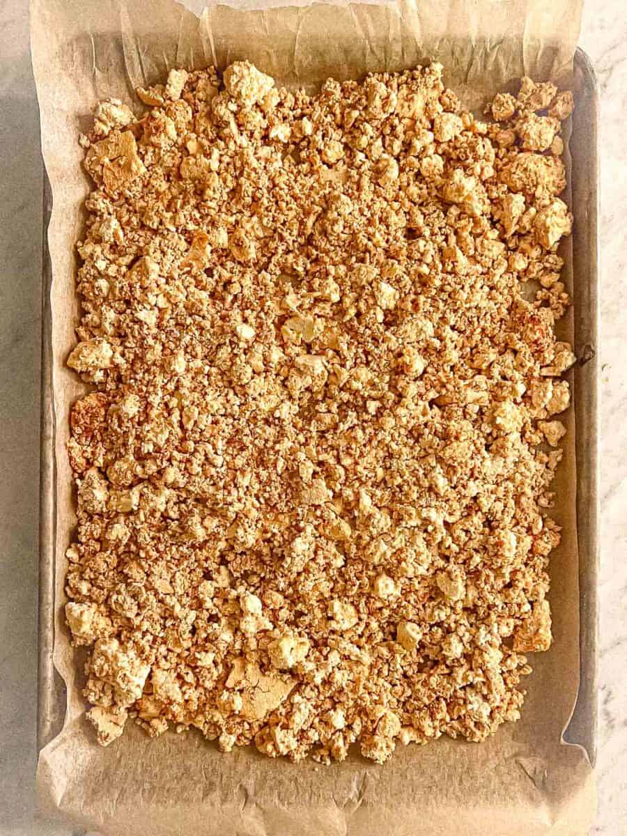 Crumbled tofu with seasonings mixed in on a cookie sheet lined with parchment paper.