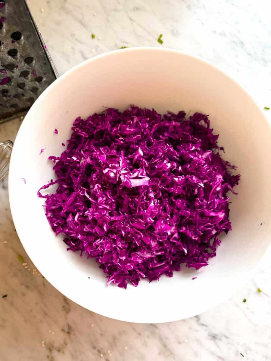 Shredded cabbage tossed in sesame ginger dressing in white bowl on countertop.