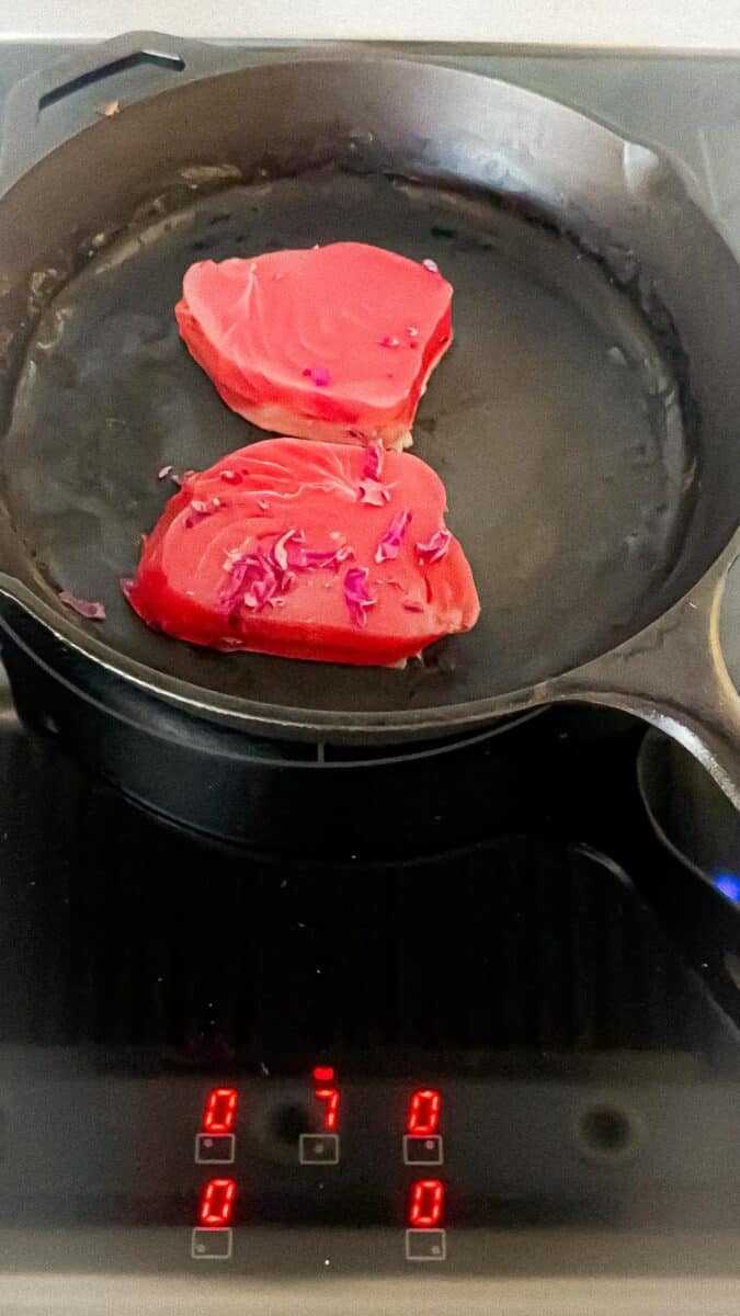 Two tuna steaks being over medium high in a cast iron skillet.