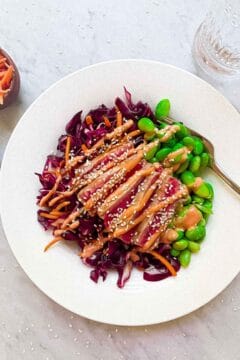 Seared ahi tuna salad in a bowl on countertop. Sesame seeds, carrot shreds, and a glass of water surround it.