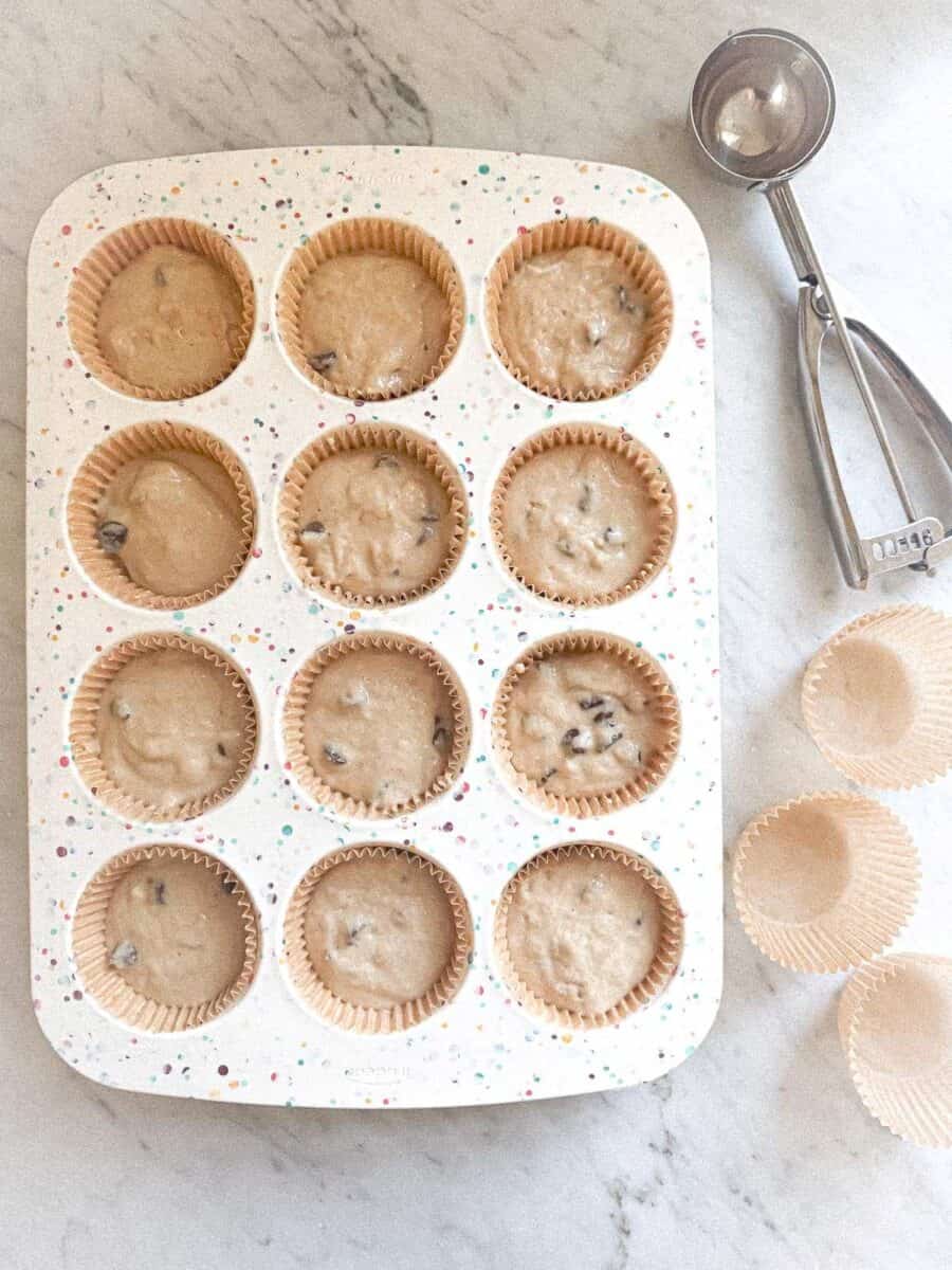 Batter in muffin cup tray with a scoop and muffin cups on a counter