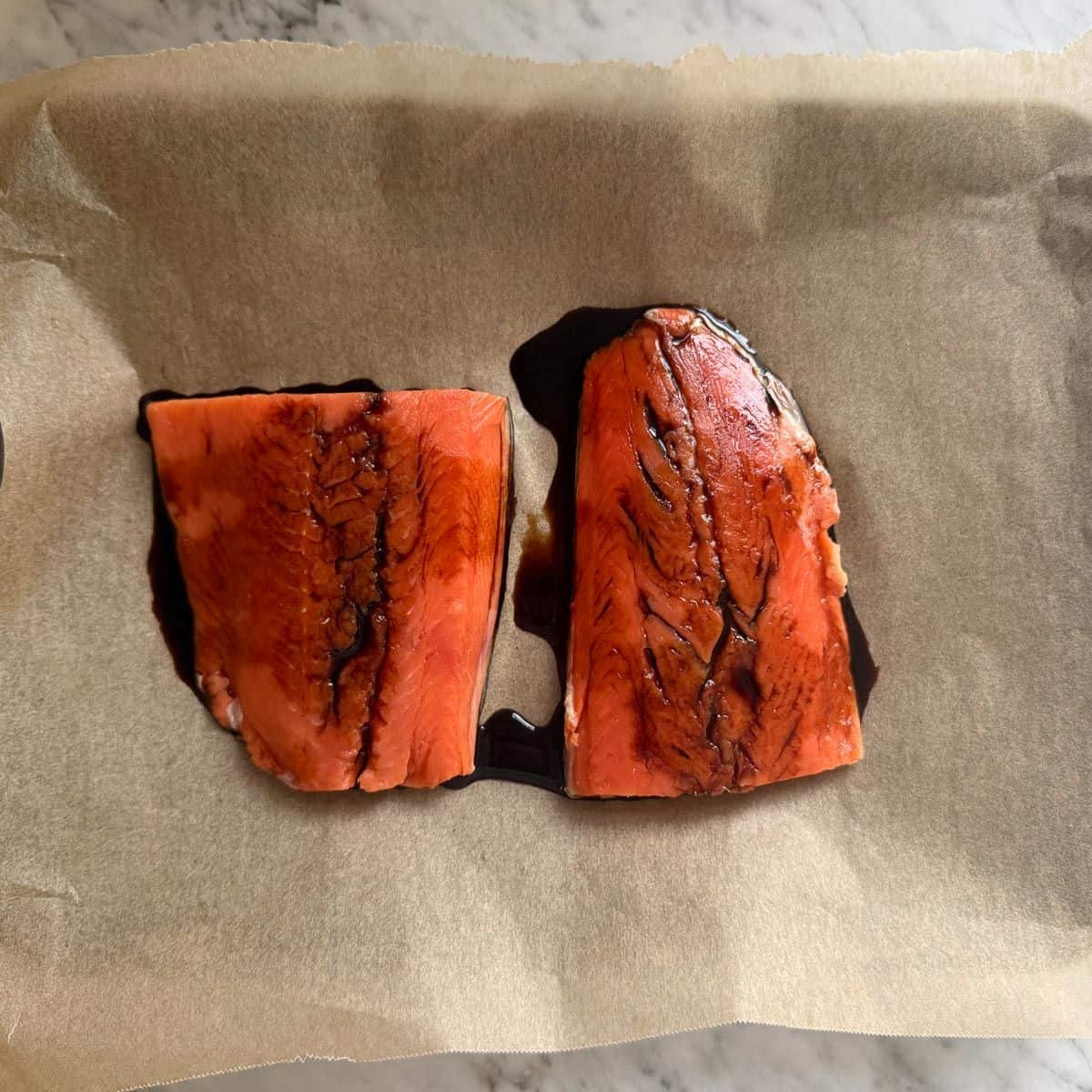 Two salmon filets on parchment paper drizzled in soy sauce.