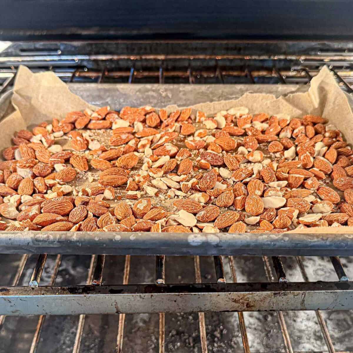 Almonds baking on a cookie sheet in the oven.