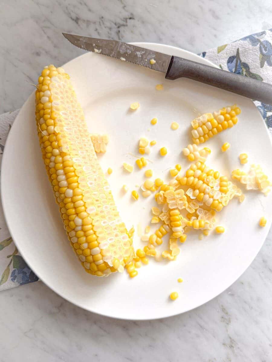 Corn on the cob with half the kernels sliced off on a plate with knife on the side.