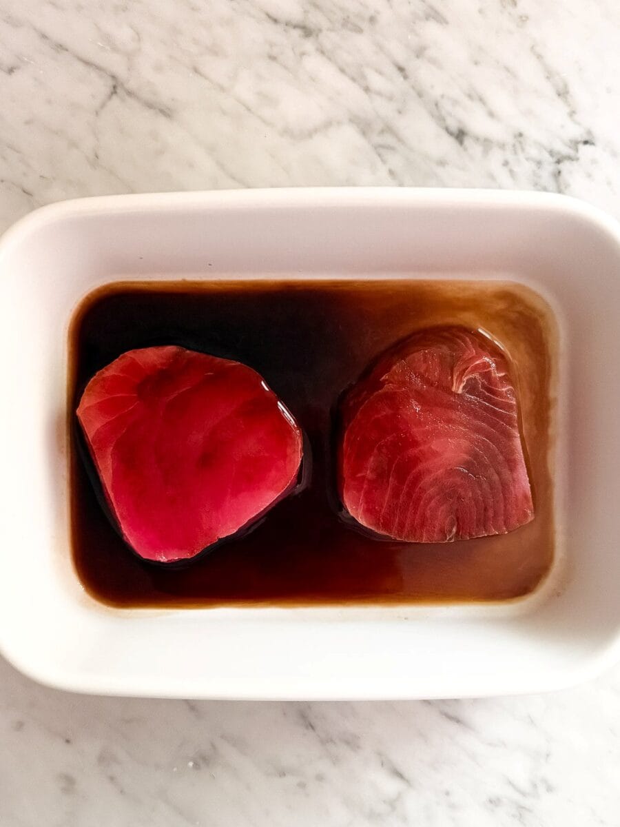 Two ahi tuna filets marinating in a white dish.
