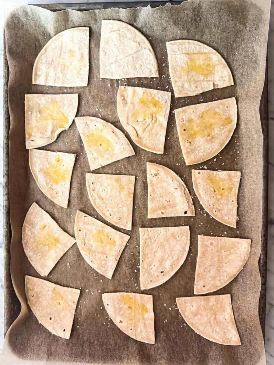 Whole wheat tortilla pieces brushed with extra virgin olive oil and sprinkled with salt on a parchment lined baking sheet.