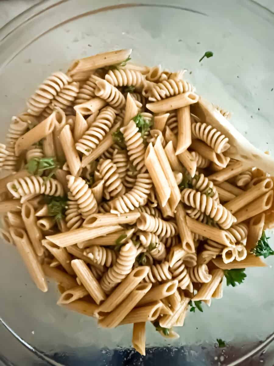 Whole wheat rotini and penne in a clear bowl with dressing and parsley.