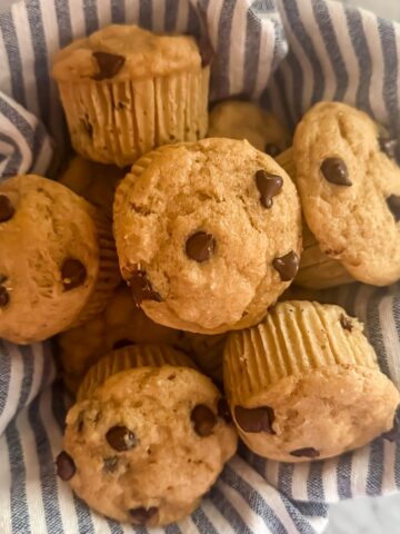 A bowl of chocolate chip protein muffins in a bowl lined with a blue and white striped linen napkin
