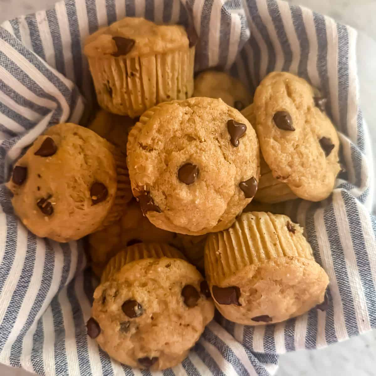 A bowl of chocolate chip protein muffins in a bowl lined with a blue and white striped linen napkin
