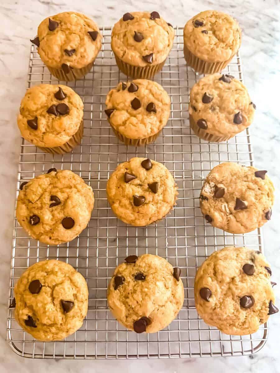 12 chocolate chip protein muffins cooling on a cooling rack which is on a marble countertop.