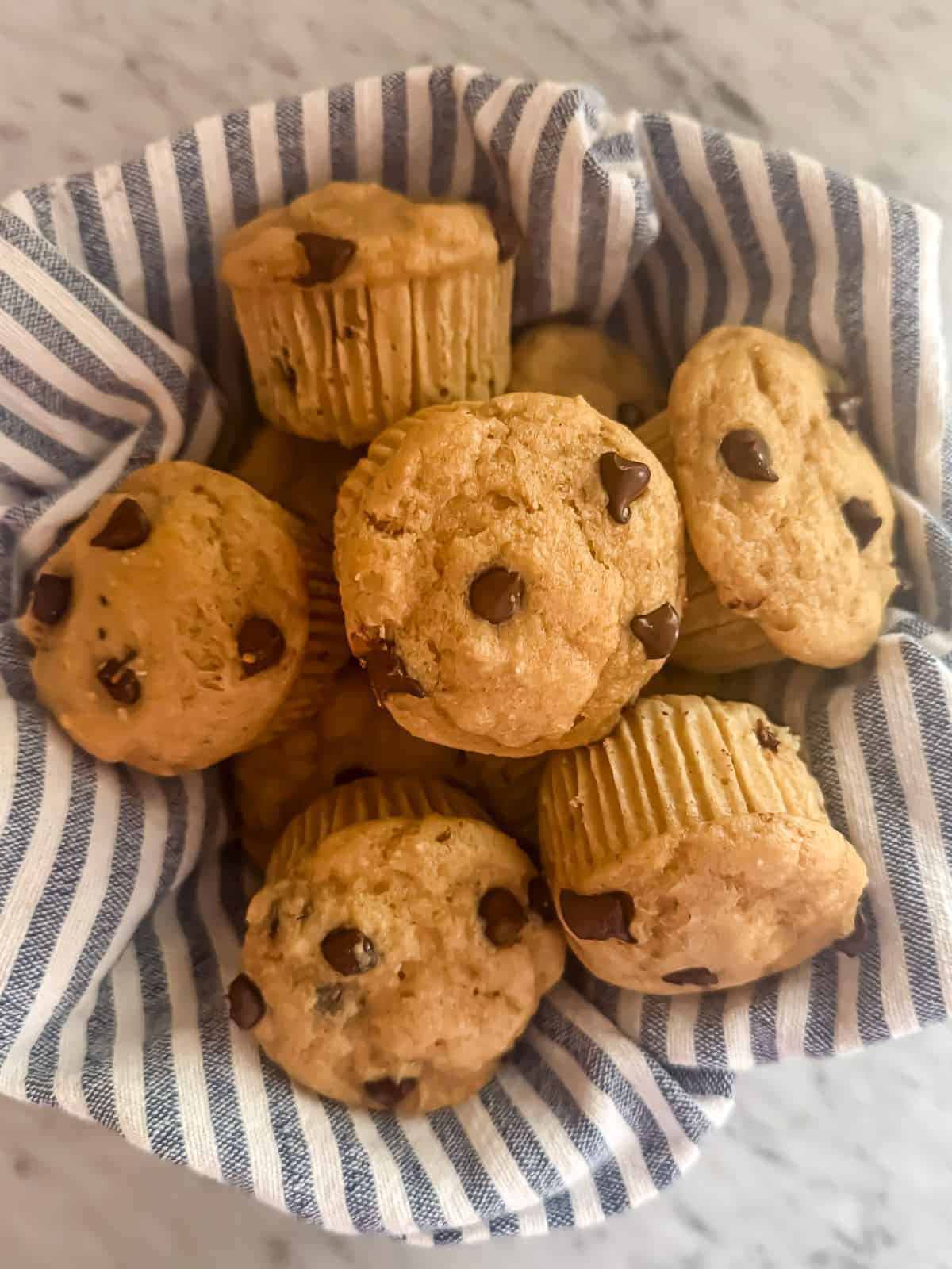 A bowl of chocolate chip protein muffins in a bowl lined with a blue and white striped linen napkin