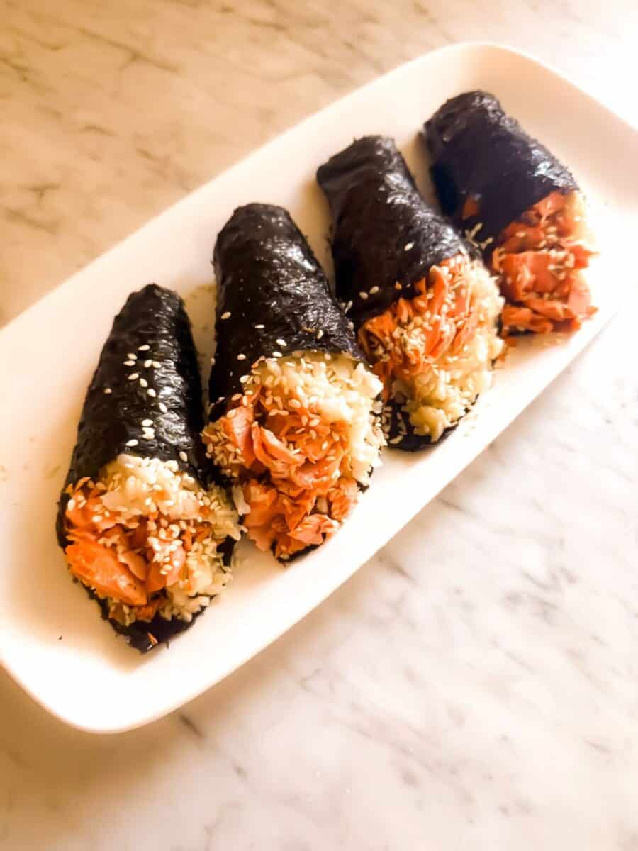 Four prepared salmon hand rolls garnished with sesame seeds on a white tray