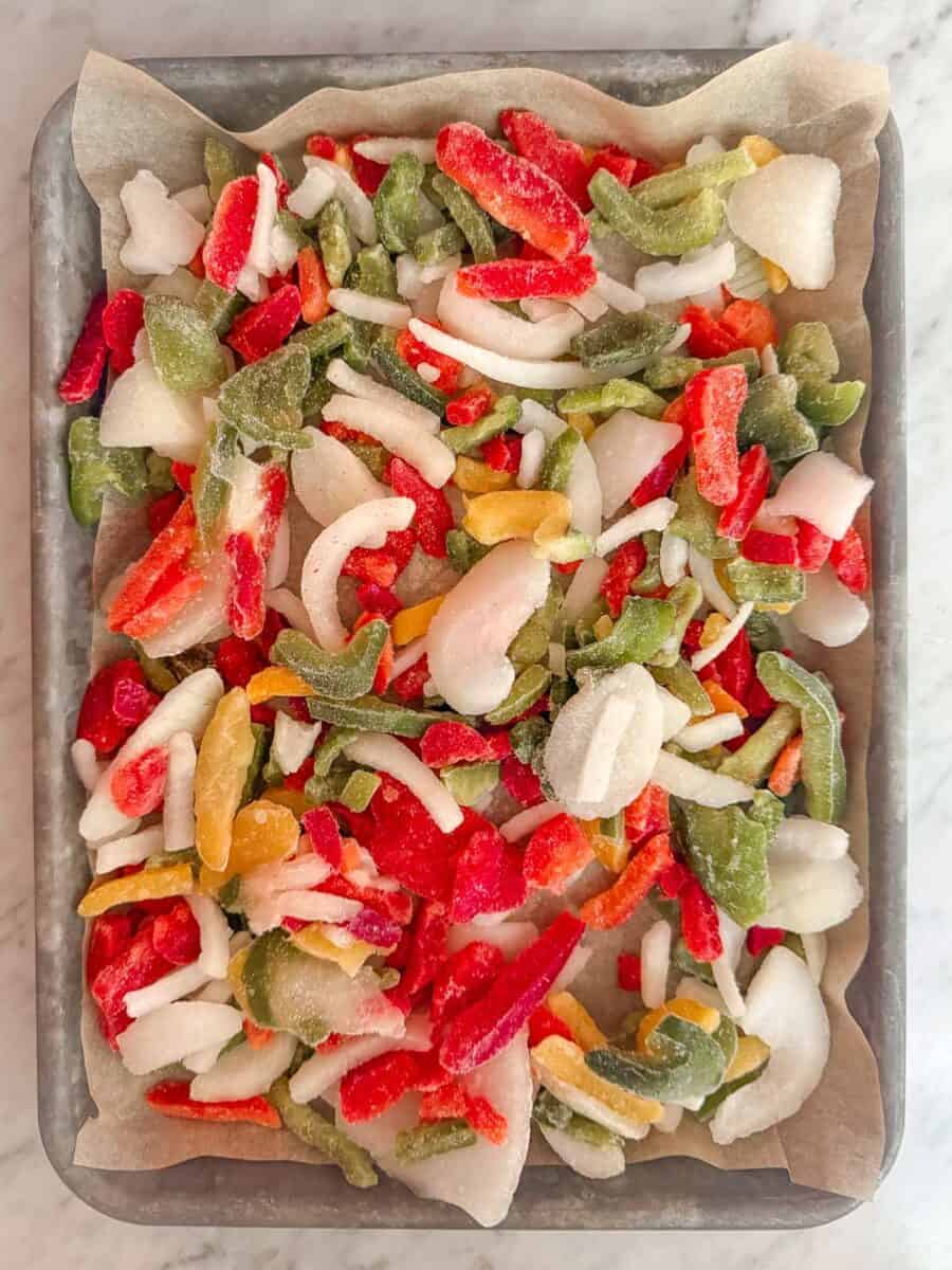 Frozen pepper and onion slices on a parchment lined baking tray.