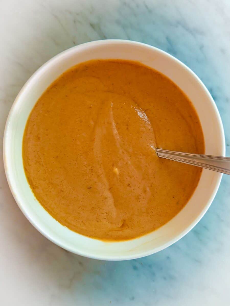 Fajita dressing ingredients mixed in a white bowl with a spoon resting on a countertop.
