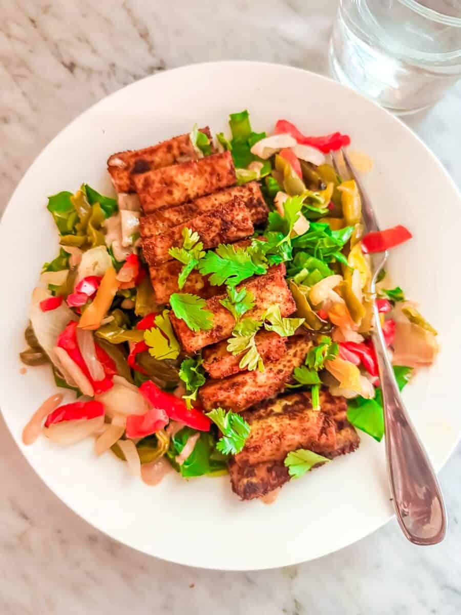 Prepared Salad with Tofu -- Fajita Edition in a bowl with a fork and glass of water next to it on a marble counter top.