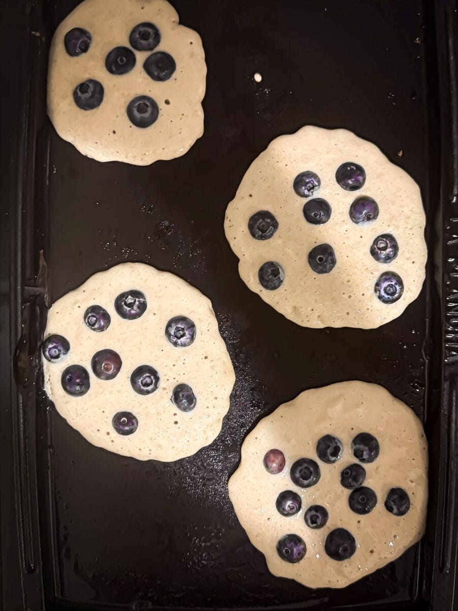 Uncooked blueberry protein pancakes on a griddle.