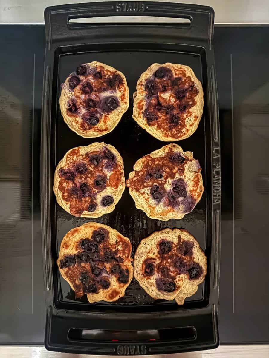 Cooked blueberry protein pancakes on a griddle atop a stove.