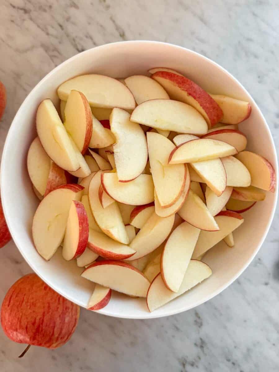 A bowl of sliced apples in a white bowl on a marble countertop.