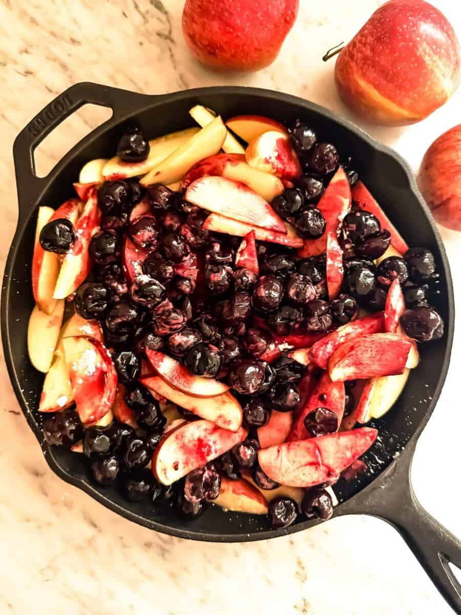 Cherries and apples in a cast iron skillet on a marble counter top.