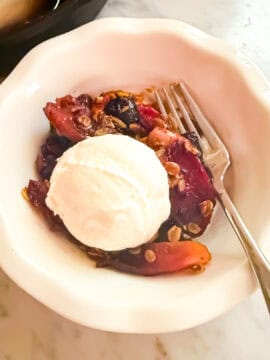 Cherry apple crisp served in a white bowl with a fork. Topped with a dallop of Greek yogurt.
