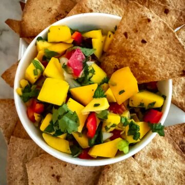 Mango jalapeno salsa in a white bowl surrounded by whole wheat tortilla chips