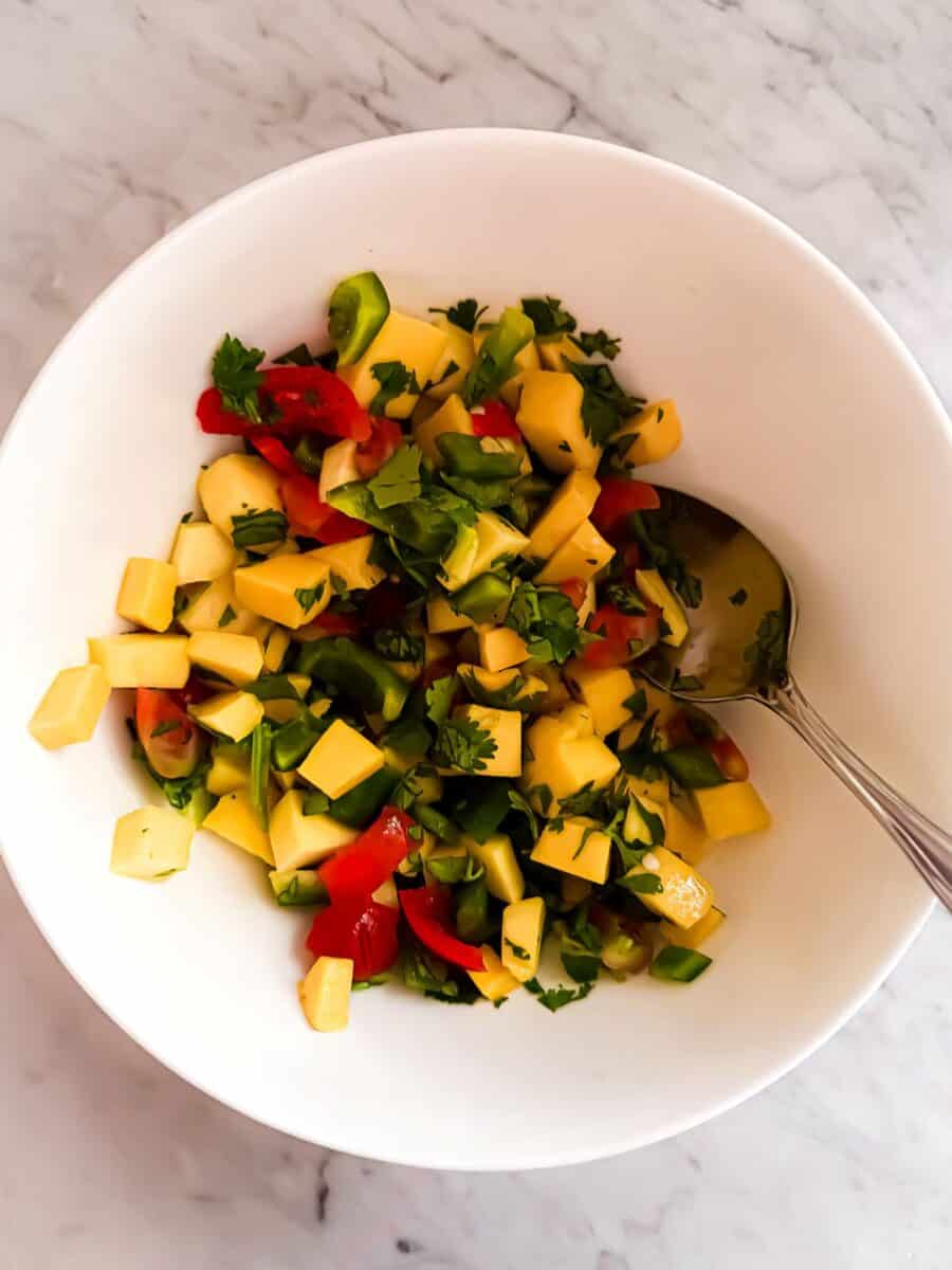 Diced mango, onion, cilantro, jalapeno and red bell pepper stirred together in a white bowl