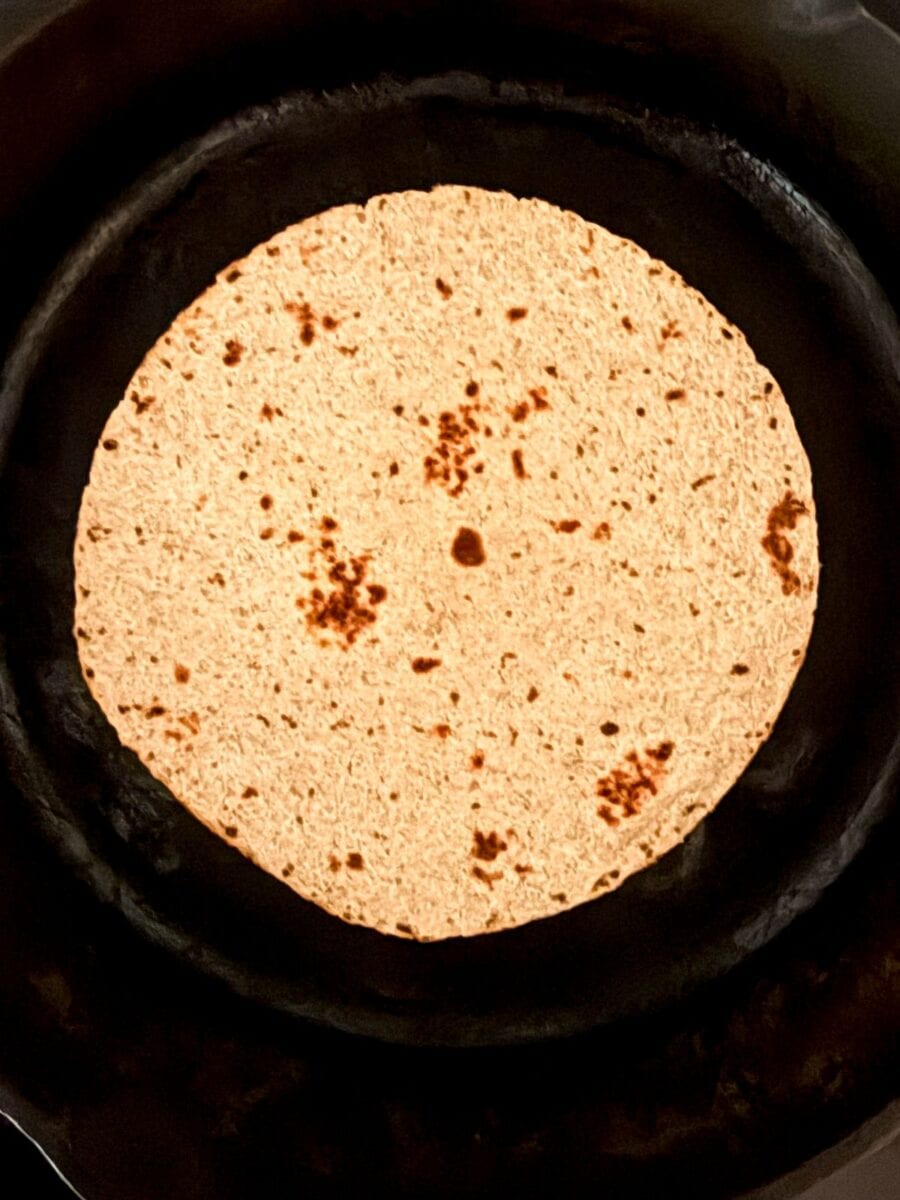 A whole wheat tortilla cooking on a cast iron skillet