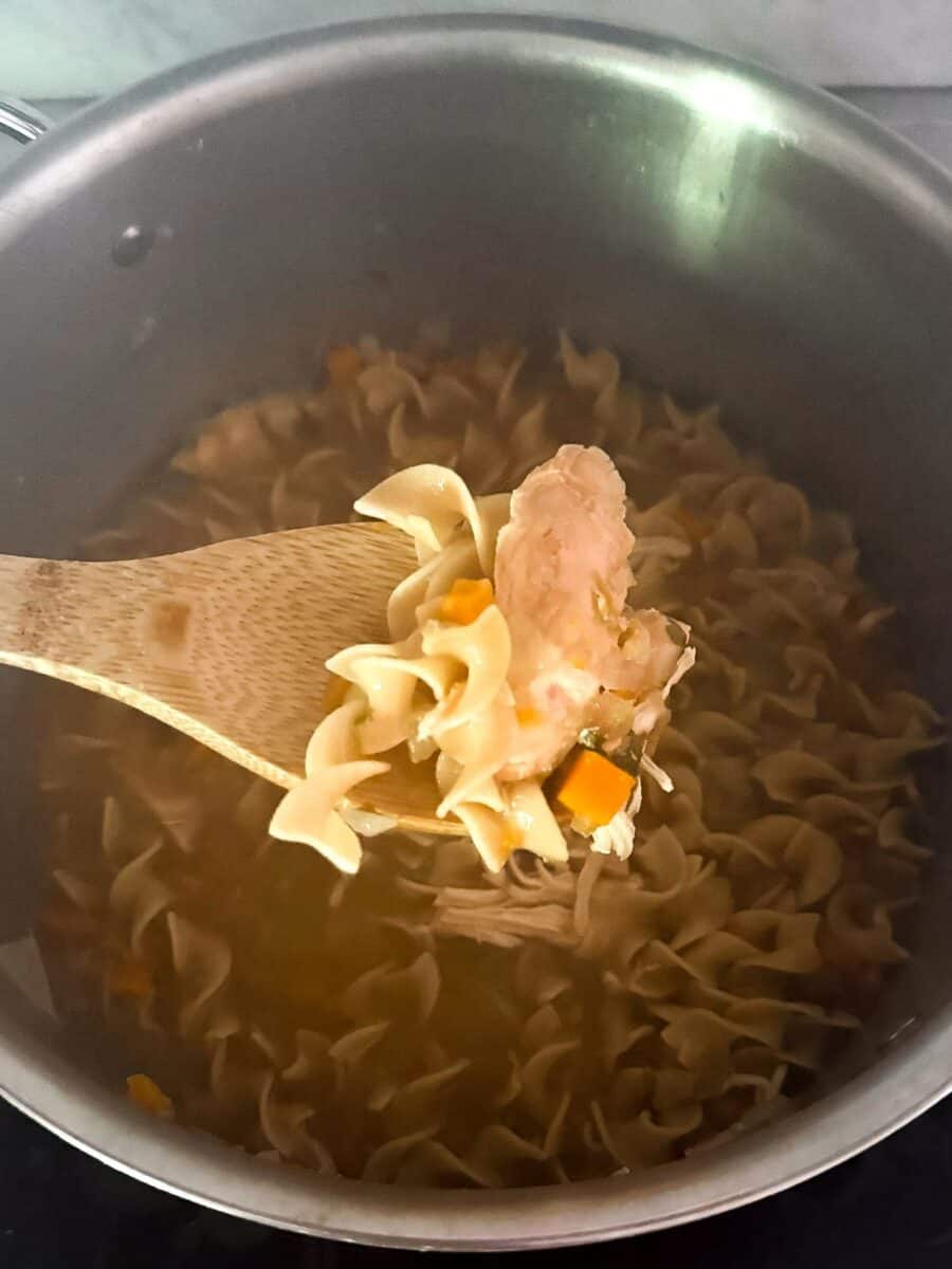 Mediterranean diet chicken noodle soup simmering in a pot, with a wooden spoon lifting a portion for serving.