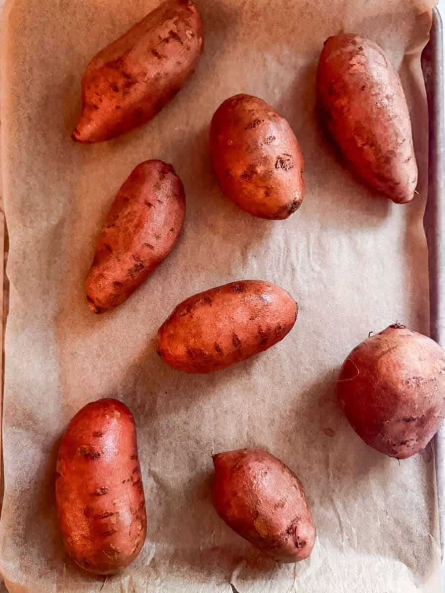 Washed sweet potatoes on a parchment lined baking sheet.