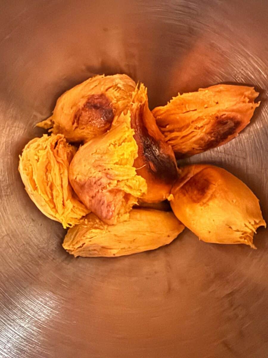 Roasted, caramelized sweet potatoes whole without skins in a silver metal mixing bowl.