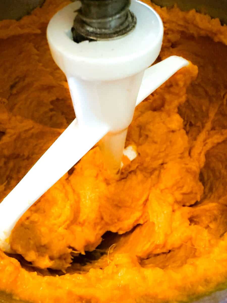 Roasted sweet potatoes in a white stand blender being whipped for gluten free sweet potato casserole.