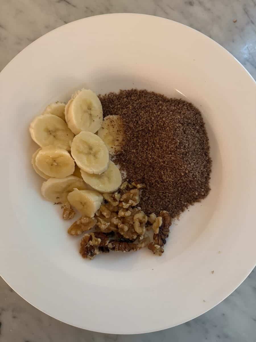 Sliced bananas, walnuts, and ground flaxseed on a white plate.