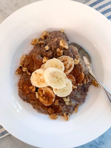 Creamy banana, flaxseed breakfast power bowl topped with walnuts, served in a white bowl. Perfect healthy omega-3 breakfast inspired by Mediterranean Diet and Portfolio Diet.