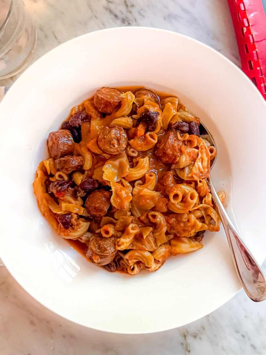 A healthier version of Portuguese Bean Soup that is Mediterranean Diet friendly in a white bowl with a spoon atop a marble countertop.