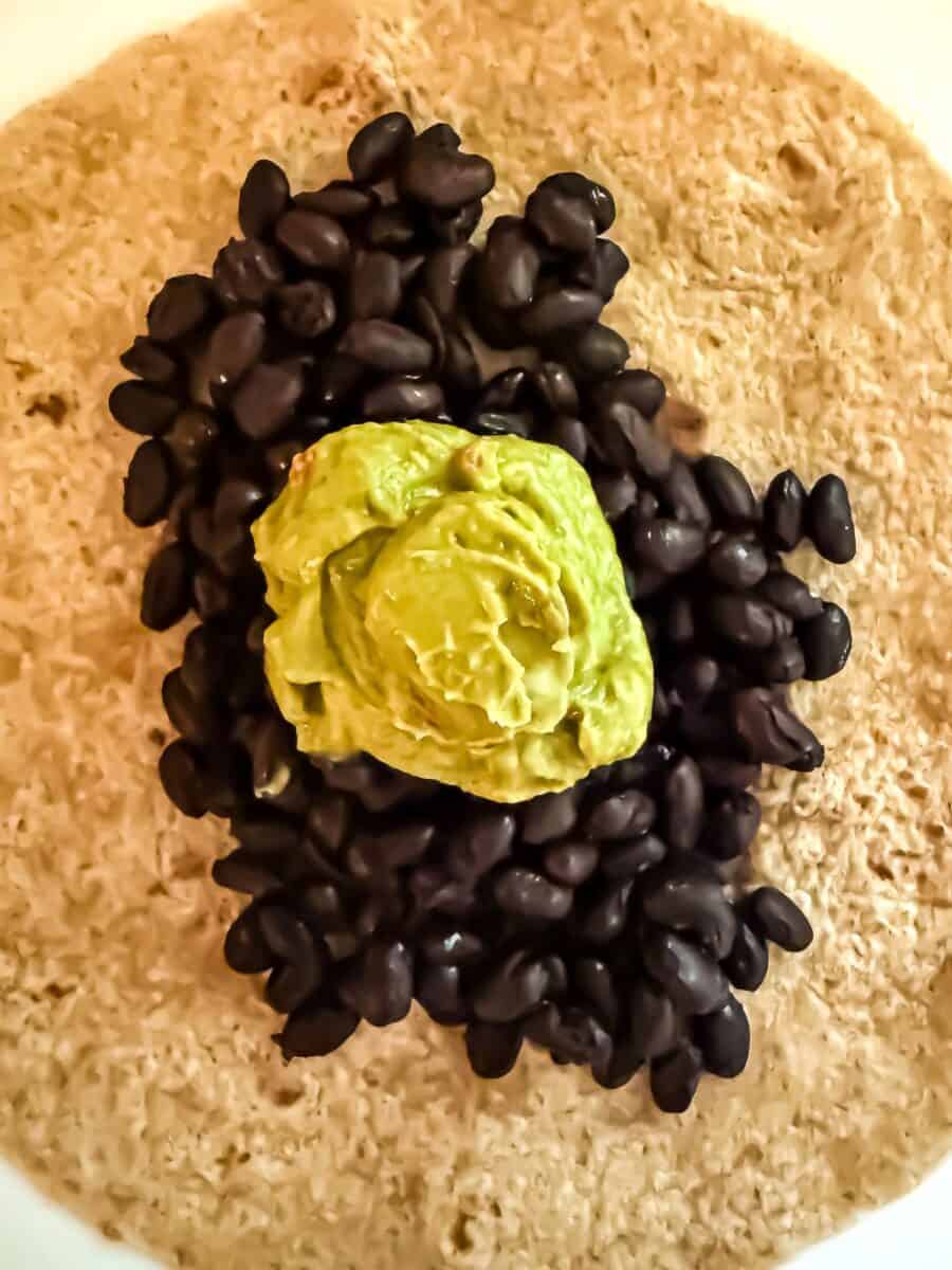 Vegan taco recipe step 3 black beans and guacamole on top of a whole wheat tortilla