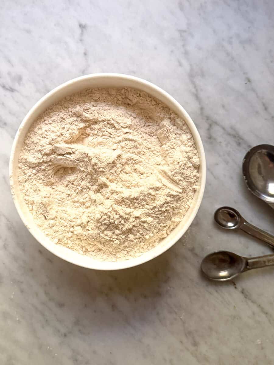 Dry ingredients in a white bowl on marble countertop with measuring spoons to the side