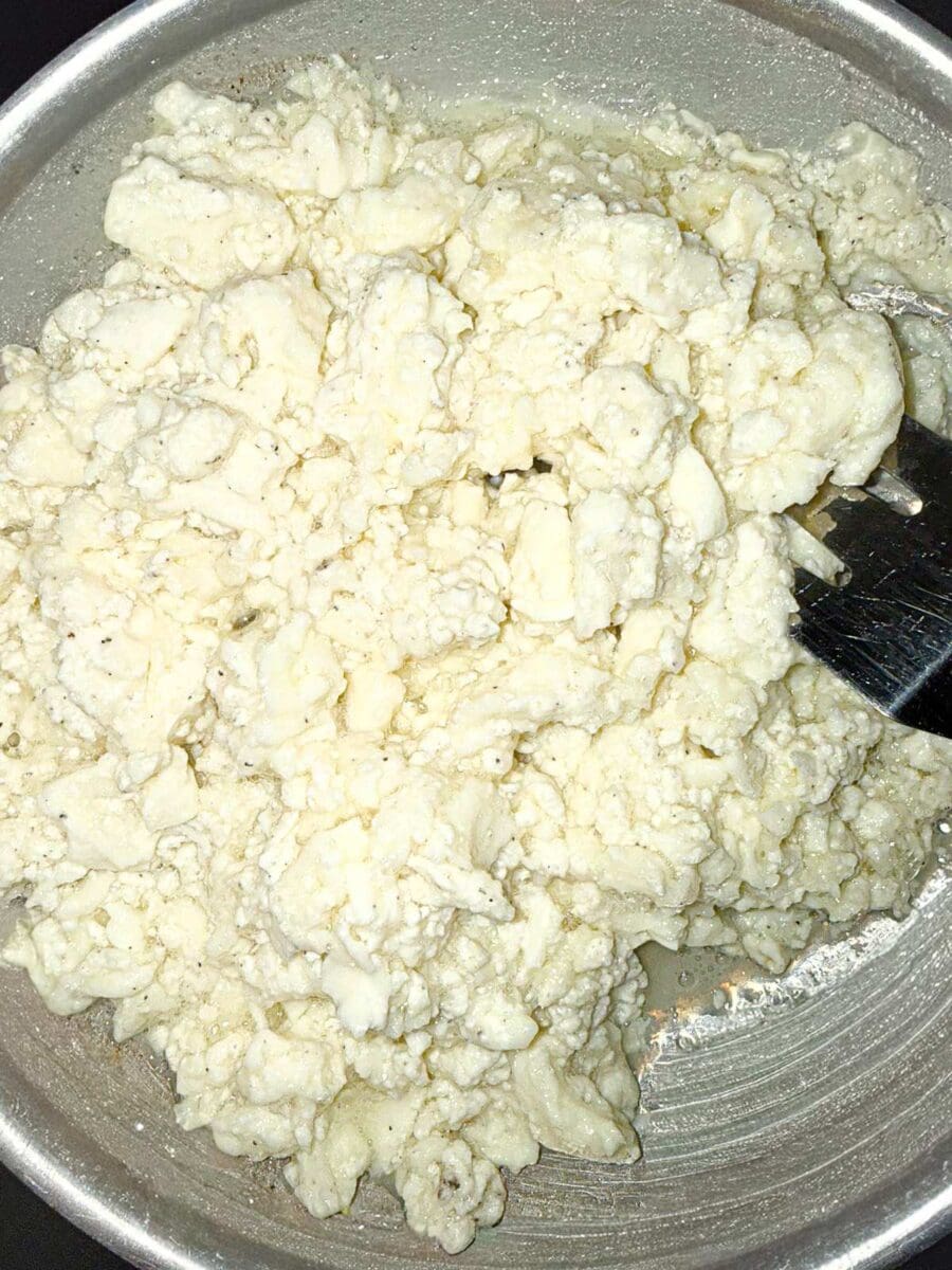 Egg whites being cooked in a stainless steel pan with a metal spatula