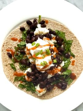 Healthy Breakfast taco made of whole wheat tortilla, egg whites, black beans, spinach, green onion, Greek yogurt on a white plate.