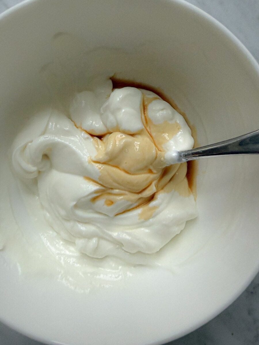 Non-fat, plain, Greek yogurt in a bowl with vanilla extract. A spoon is in the bowl.