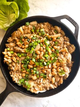 Tofu with brown sauce, green onions, water chestnuts, and peanuts prepared for Tofu Lettuce Wraps in a cast iron skillet on a marble countertop.