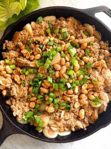 Tofu with brown sauce, green onions, water chestnuts, and peanuts prepared for Tofu Lettuce Wraps in a cast iron skillet on a marble countertop.