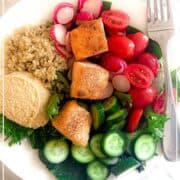 Mediterranean Hummus Bowl with leafy greens, tomatoes, salmon, quinoa, cucumbers and an evoo dressing in a bowl with a fork. Overlay text says Mediterranean Diet Hummus Bowl with the Mediterranean for Life logo