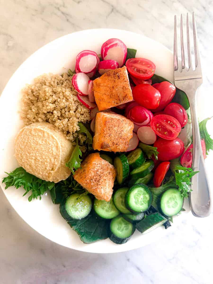 A Mediterranean Diet salad with hummus, salmon, quinoa, tomatoes, cucumbers, radishes and spring mix.