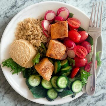 A vibrant Mediterranean Diet hummus salad featuring salmon, cherry tomatoes, cucumbers, radishes, quinoa, and fresh greens, perfect for a healthy diet.