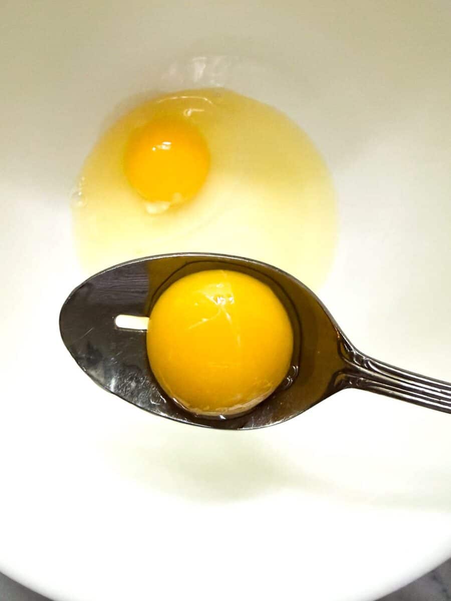 Two eggs in a white bowl. Yolk is shown being separated so that only egg whites are used for the recipe to keep protein while reducing saturated fat content.