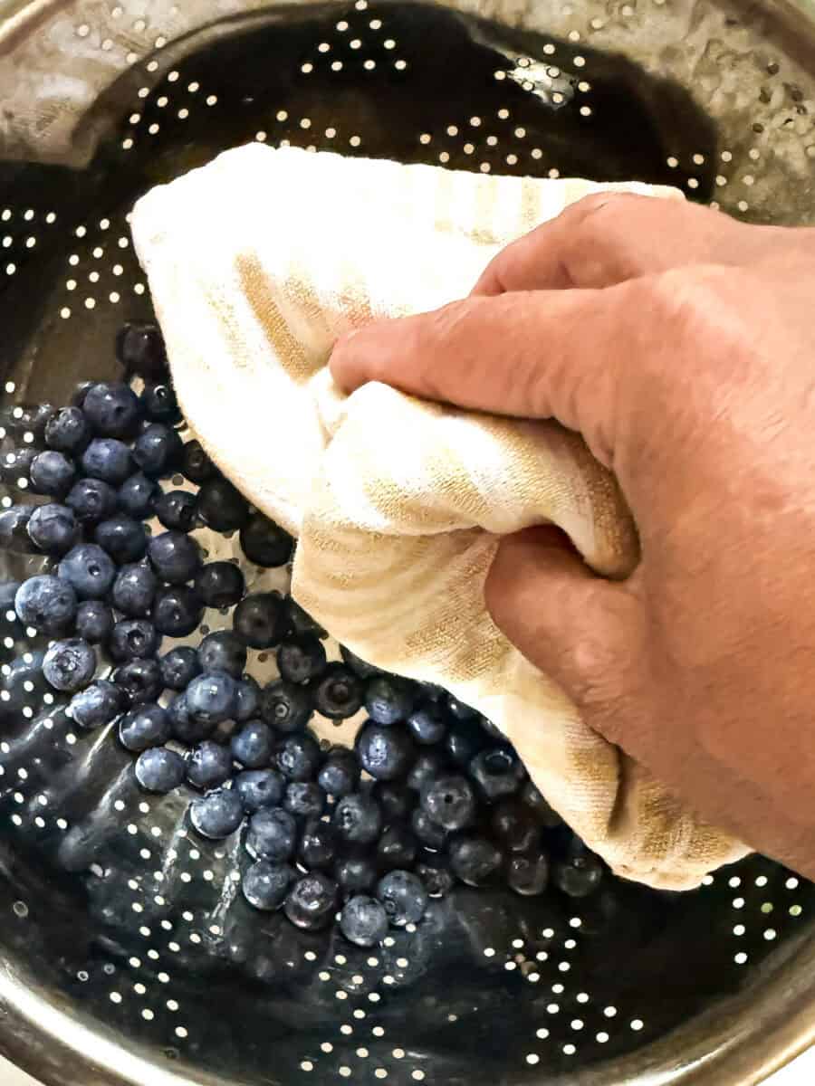 Freshly rinsed blueberries in a colander being patted dry