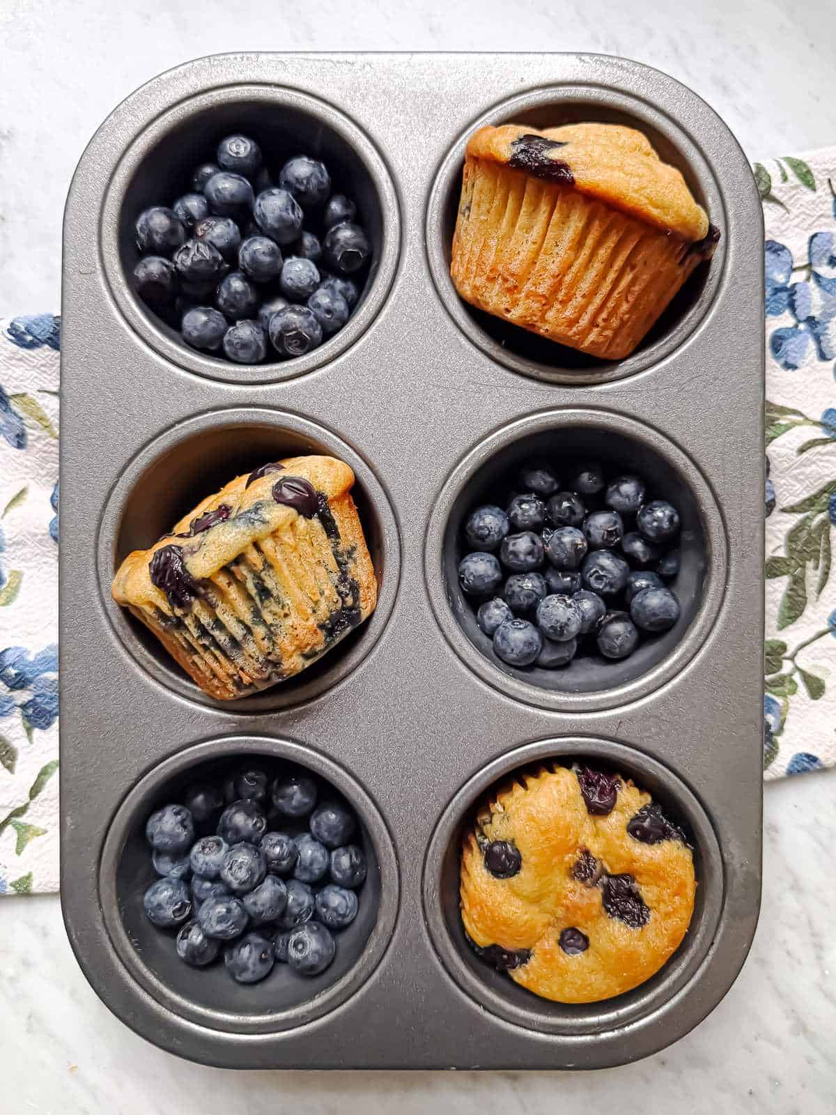 Three high protein blueberry muffins in a muffin tin with the remaining three spots full of blueberries.